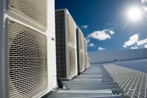 Multiple air conditioning systems are lined up in a row on a commercial rooftop.