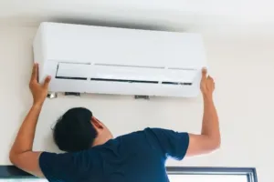 An AC repair technician is looking behind a ductless mini split unit. 