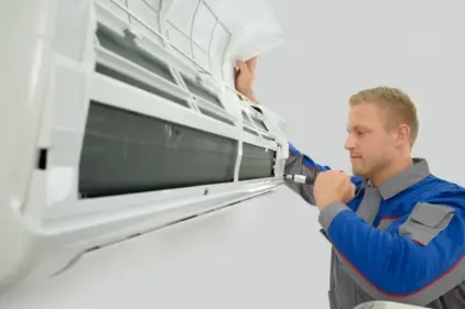 A photo of an AC technician working with a screwdriver on an AC unit.