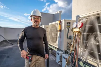An hvac technician standing pridefully near his completed work.