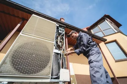 An HVAC repairman standing next to a double stacked unit while repairing it.